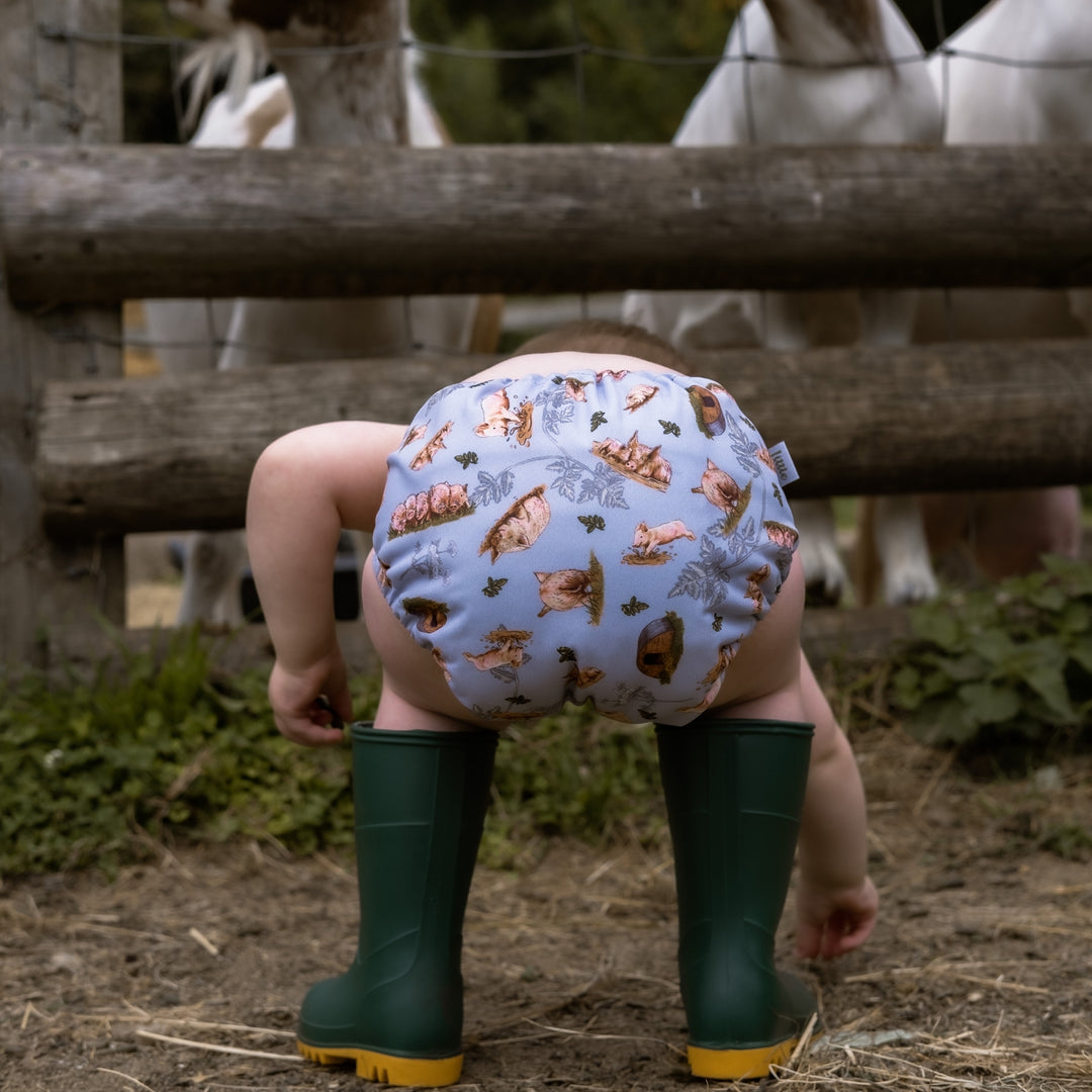 Baby wearing Onesize Reusable Pocket Nappy with Pig Print by LittleLamb and Wellington Boots#color_sow-in-love