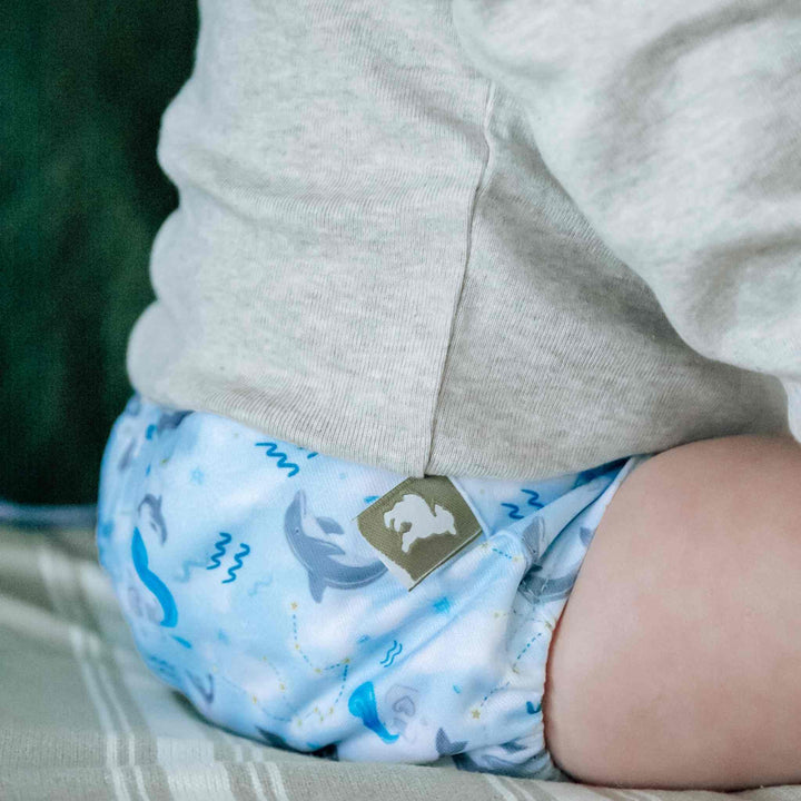Aquarius Onesize Pocket Nappy by LittleLamb - blue nappy with dolphins and Aquarius star signs  - on a baby