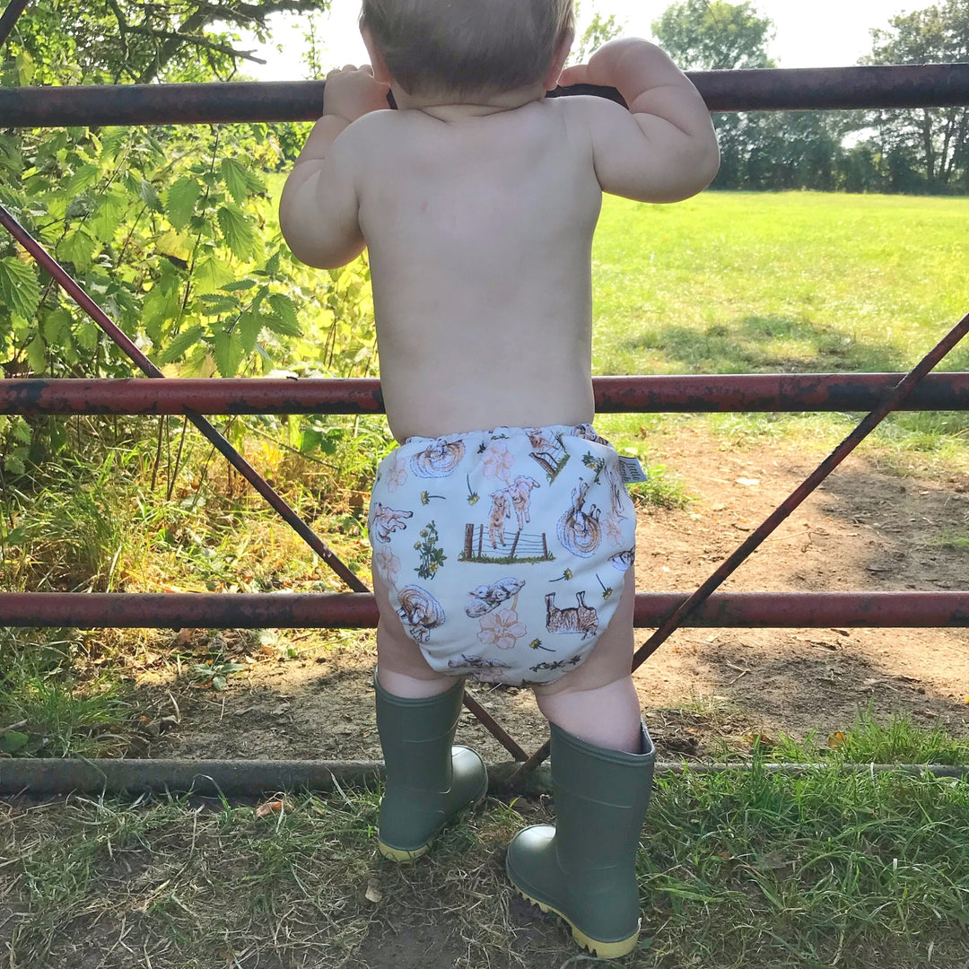 Little baby wearing wellington boots, looking through a gate into a field, wearing Onesize Reusable Pocket Nappy with Sheep illustrations by LittleLamb#color_loving-ewe